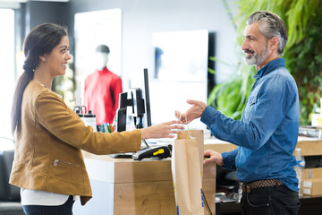 sales clerk passing purchase to customer in paper bag