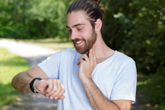 young man checking pulse after workout in park