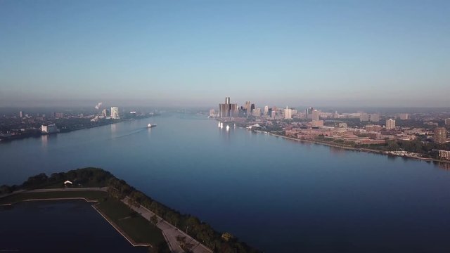 View of the Detroit skyline from Belle Isle on the Detroit river. Lake freighter passing by on a sunny summer day with blue sky. Aerial drone video of Michigan.

