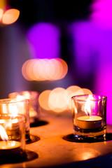 Flame of many candles burning on purple blurred background.