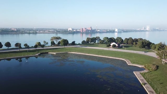 View of the Detroit skyline from Belle Isle on the Detroit river. Lake freighter passing by on a sunny summer day with blue sky. Aerial drone video of Michigan.
