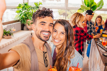 Young happy smiling couple making selfie during a party with friends - mix raced group of young...
