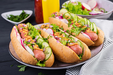 Hot dog with  sausage, cucumber, radish and lettuce on dark wooden background. Summer hotdog.