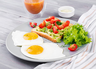 Fototapeta na wymiar Breakfast. Fried egg, vegetable salad and a grilled avocado sandwich on a grey background.