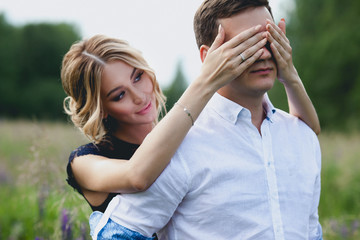 Happy loving couple in a field with lupines flowers, the girl covers eyes with a man. surprise game