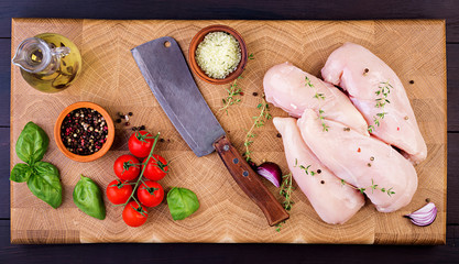 Raw chicken breast fillets on wooden cutting board with herbs and spices. Top view