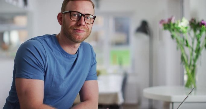 4K Portrait attractive man with glasses working on laptop & turning to smile at camera. Slow motion