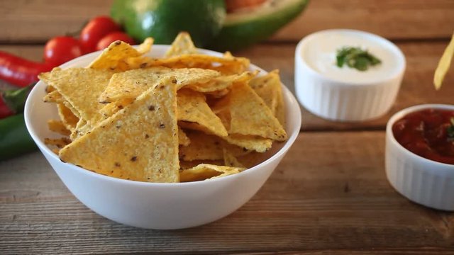 Woman hand takes Mexican chips nachos and dips in a sause salsa