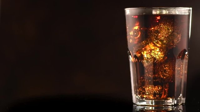 Coke with ice cubes closeup. Glass of fizzy cola rotated over brown background. Slow motion 4K UHD video footage. 3840X2160