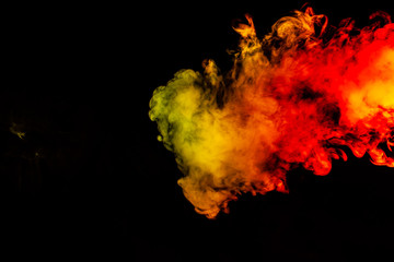 Beautiful horizontal column of smoke in the neon bright light of red, green, yellow and orange on a black background exhaled out of the vape. Nice pattern for printing and backdrop of colored waves.