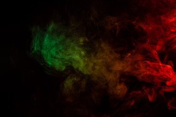 Beautiful horizontal column of smoke in the neon bright light of red, green, yellow and orange on a black background exhaled out of the vape. Nice pattern for printing and backdrop of colored waves.