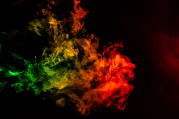 Beautiful horizontal column of smoke in the neon bright light of red, green, yellow and orange on a black background exhaled out of the vape. Nice pattern for printing and backdrop of colored waves.