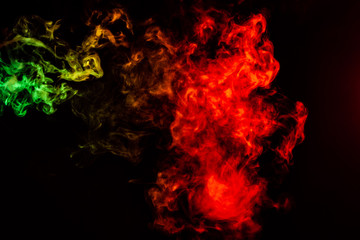 Beautiful horizontal column of smoke in the neon bright light of red, green, yellow and orange on a black background exhaled out of the vape. Nice pattern for printing and backdrop of colored waves.