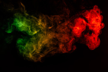 Beautiful horizontal column of smoke in the neon bright light of red, green, yellow and orange on a black background exhaled out of the vape. Nice pattern for printing and backdrop of colored waves.