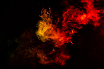Beautiful horizontal column of smoke in the neon bright light of red, green, yellow and orange on a black background exhaled out of the vape. Nice pattern for printing and backdrop of colored waves.
