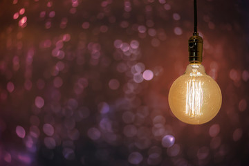 An old vintage electric light bulb hanging in the air on a blurry tungsten background. Detail shot...