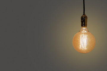 An old vintage electric light bulb hanging in the air on a grey background. Detail shot of a glass...
