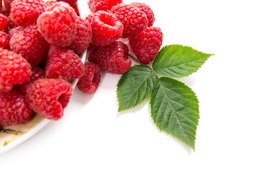 Small plate with ripe raspberries and green leaf isolated on white background.