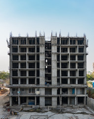 construction site of a modern tall residential building with workers working in the apartment block with the steel rods scattered on the ground.