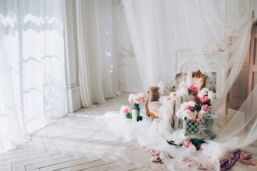 vintage armchair decorated with peonies  flowers and greens, stands in a classic room on a white wooden floor surrounded by candles near large window and curtains