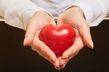 Hände halten rotes Herz als Symbol für Pflege