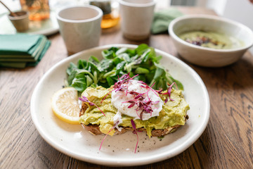 Morning in cafe, oak table. Healthy breakfast with wholemeal bread toast with avocado, poached egg with green salad. Green tea on the Background.