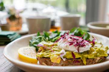 Morning in cafe, oak table. Healthy breakfast with wholemeal bread toast with avocado, poached egg with green salad. Green tea on the Background.