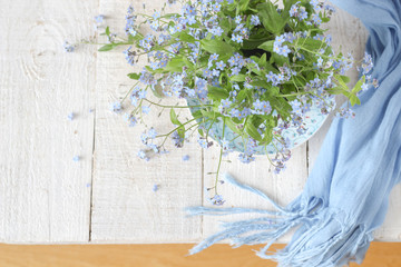 Still life with tiny spring flowers - forget-me-nots in blue vases on a white wooden table