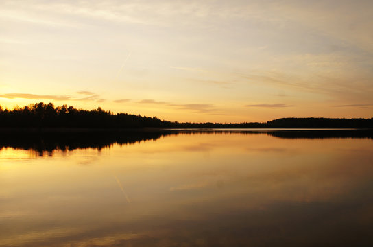 Beautiful sunset on the forest lake. The sun is reflected in the water. Bright contrasting sky. © Payllik
