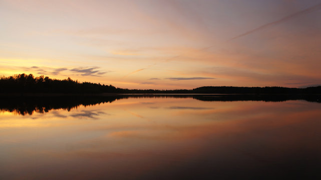 Beautiful sunset on the forest lake. The sun is reflected in the water. Bright contrasting sky. © Payllik