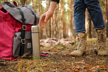 Woman with backpack and thermos traveling in forest