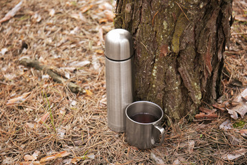 Fototapeta premium Thermos and mug of tourist near tree in forest