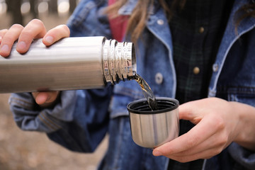Woman drinking hot tea from thermos outdoors
