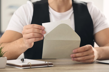Young man opening envelope with invitation at home, closeup