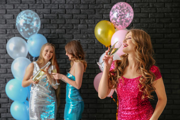 Beautiful young women with glasses of champagne and balloons near dark wall