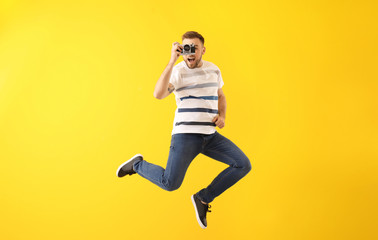 Jumping young man with photo camera on color background