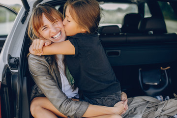 Fashionable mother with daughter. Family is sitting in the trunk. Girl in a black t-shirt