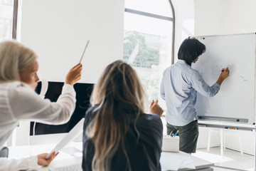 Dark-haired man drawing infographic on flipchart standing in conference hall. Portrait from back of...