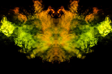 Smoke of different green, yellow, orange and red colors in the form of horror in the shape of the head, face and eye with wings on a black isolated background. Soul and ghost in mystical symbol