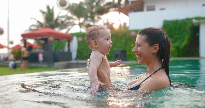 Young mother with 8 month old son in pool. Baby likes to swim, he slaps his hands on the water and laughs. in slow motion. Shot on Canon 1DX mark2 4K camera