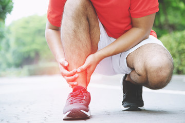 Runner touching painful twisted or broken ankle. Athlete runner training accident. Sport running ankle sprained sprain cause injury knee. and pain with leg bones.  Focus red legs on to show pain. 