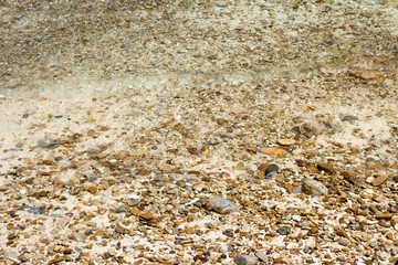 Soft waves with foam of water on pebbles and sandy beach.