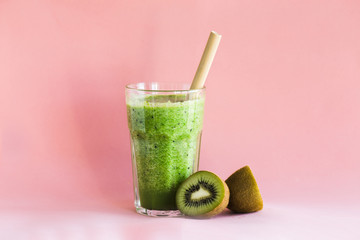 Healthy green smoothie in a glass cup on pink background