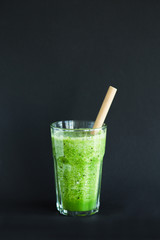 Healthy green smoothie in a glass cup on a black background