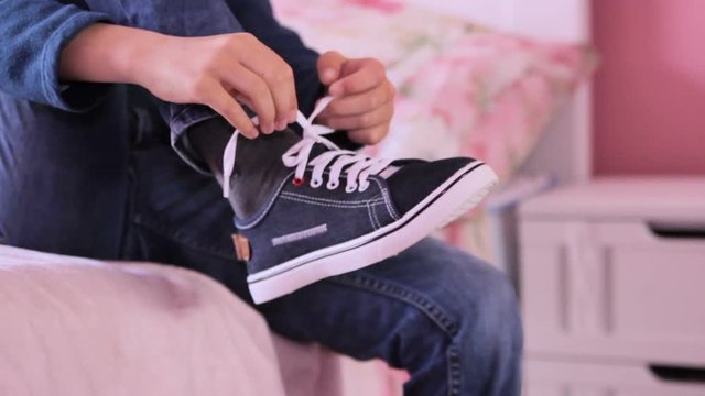 Boy Takes Off Plimsoll Shoe,the schoolboy came from school to the bedroom and dropped sneakers, sit on the bed and unleashed lacing