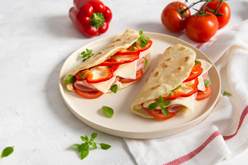 Italian piadina romagnola flatbread with red pepper, tomatoes, prosciutto ham, cheese and basil on the plate on white wooden background. Copy space