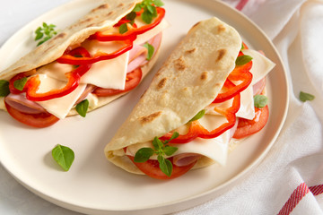 Piadina romagnola - Italian flatbread with prosciutto, tomato, basil, pepper and cheese on white background. Close up
