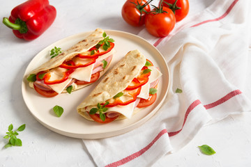 Italian piadina romagnola flatbread with red pepper, tomatoes, prosciutto ham, cheese and basil on the plate on white wooden background. Italian restaurant cuisine. Copy space