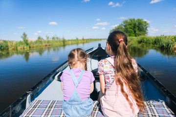 Fototapeta na wymiar Back view of happy two girl with long hair sit on a boat ride at the river. Enjoying a lovely summer day.