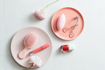 Makeup products on pink plate on white background